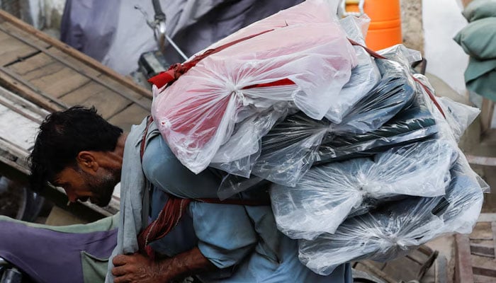 A labourer bends over as he carries packs of textile fabric on his back to deliver to a nearby shop in a market in Karachi on June 24, 2022. — Reuters