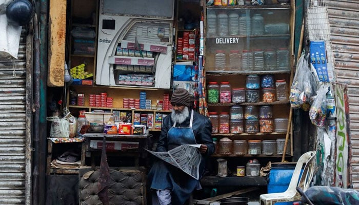 A man reads newspaper while selling betel leaves, known as pan, cigarettes and candies from a shop in Karachi on December 30, 2021. — Reuters